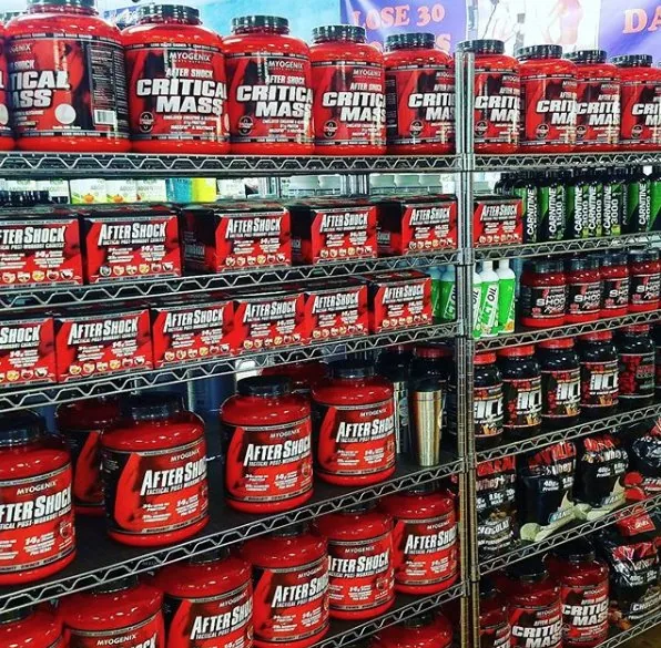 Metal shelving displaying red containers of Critical Mass and AfterShock supplement products in a vitamin store.